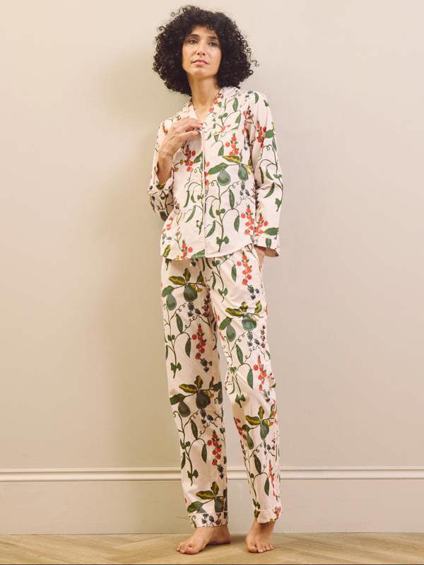 Woman wearing a pear & floral pyjama set against a plain wall.