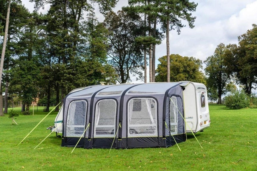 The OLPRO View 420 Caravan Inflatable Porch Awning With Porch Extension attached to a caravan at a campsite with a treeline in the background.