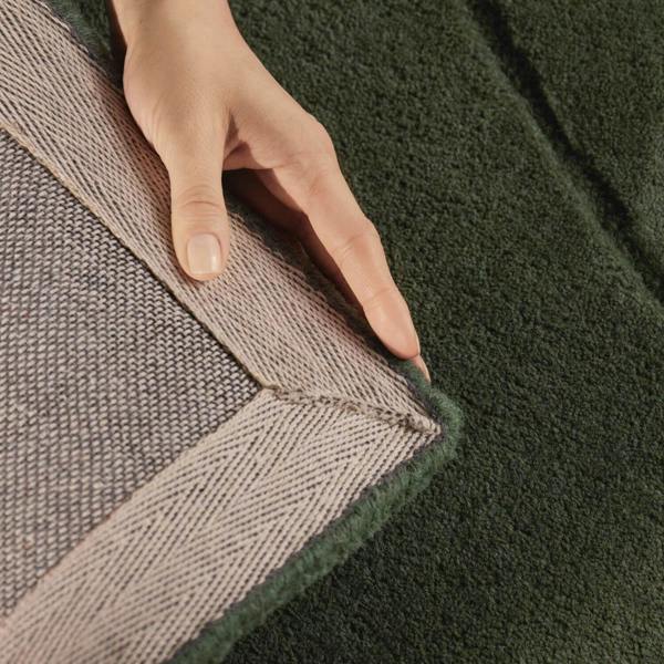 Close-up of a hand touching the edge of two different textured rugs.