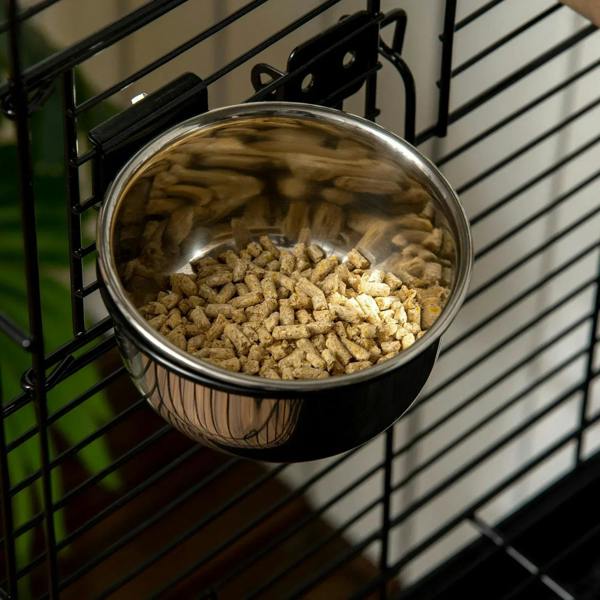Stainless feed bowl attached to black cage bars filled with bird pellets