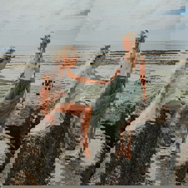 Two girls sitting on rocks by the ocean, holding hands.