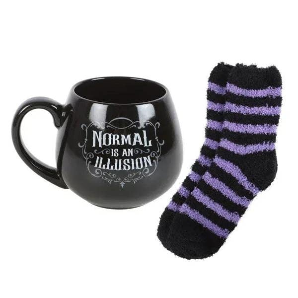 Black mug with purple-striped socks beside it and 'Normal is an Illusion' print