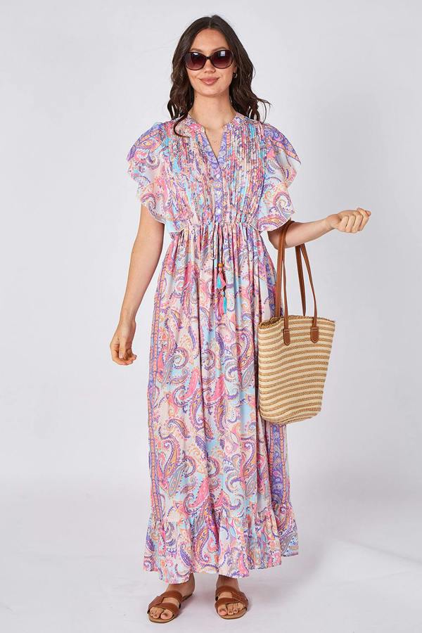 Woman wearing a colorful patterned dress holding a straw bag on a white background