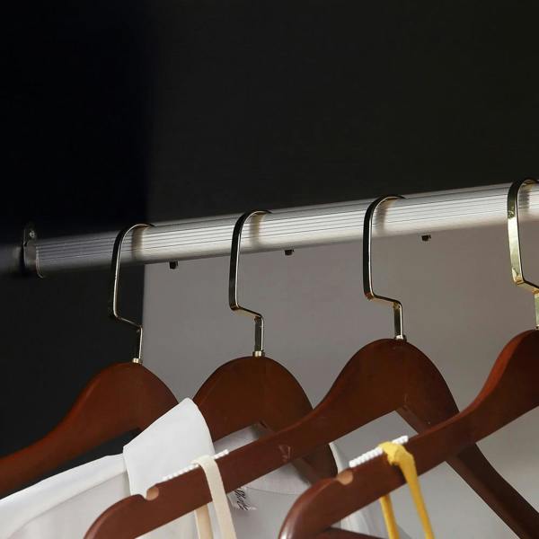 Clothes on brown hangers on a silver hanging rail inside a black wardrobe