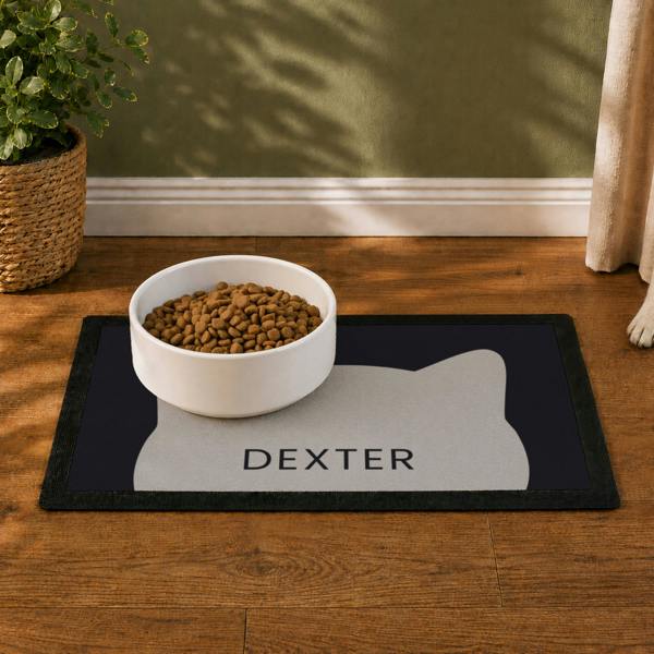 Black personalised cat bowl mat featuring a grey cat silhouette graphic and the name DEXTER, topped with a white bowl filled with food.