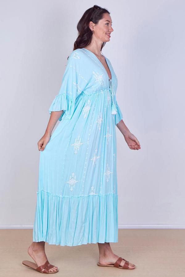 Woman wearing a light blue dress with floral patterns on a plain background