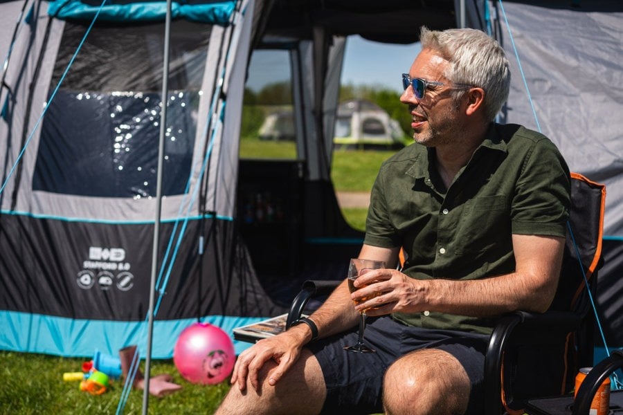 A man sits outside the Stafford 8.0 8 berth tent in an OLPRO camping chair, he is talking to someone