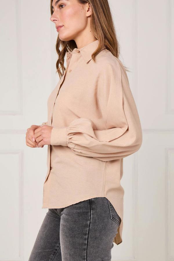 Woman wearing a beige blouse and gray pants against a white background