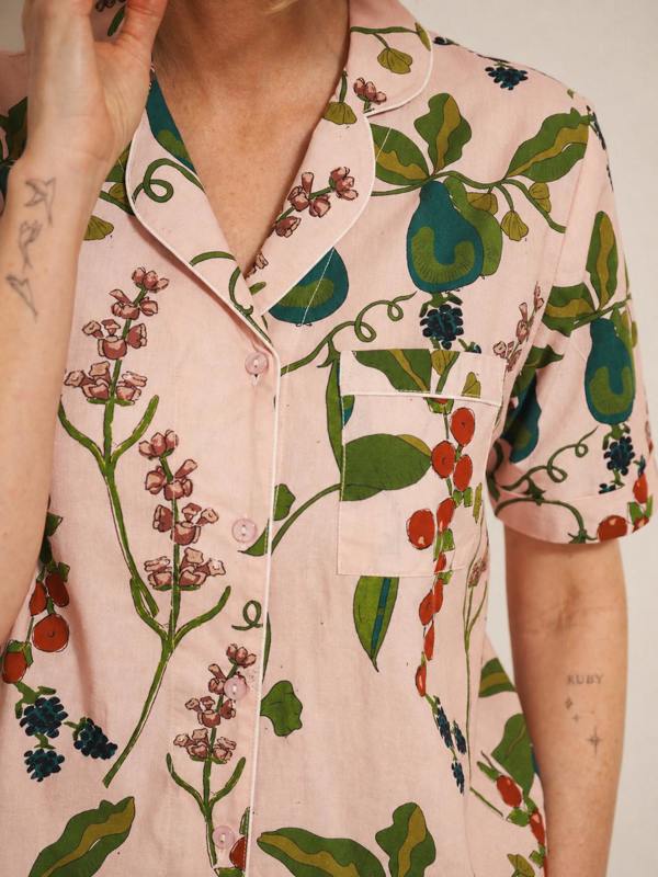 Person wearing a pink floral patterned pyjama shirt with green leaves and red berries.