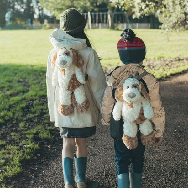 An adorable children's plush puppy backpack made from soft brown and white fabric with floppy ears, closed eyes, and a small black nose, displayed against a clean background.