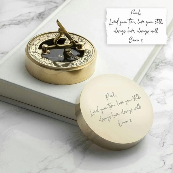 A brushed brass Personalised Handwriting Romantic Sundial Compass showing an engraved romantic note on the lid next to a white book.
