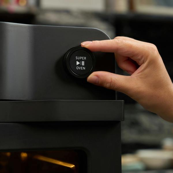 A hand presses the Super Oven button with play/pause symbols on the Fridja f66 Super Oven – a modern black 15L digital air fryer oven with advanced convection cooking.
