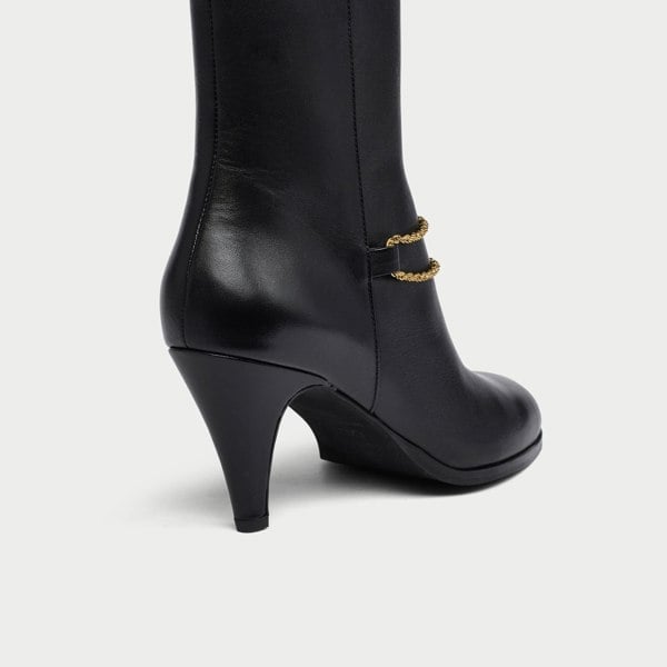 Black Maya boot with gold chain detail on a white background heel close-up
