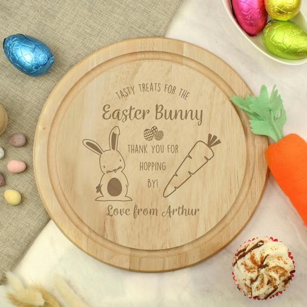 A round wooden Easter treat board engraved with 'Love from Arthur', styled with chocolate eggs, a toy carrot, and a cupcake.