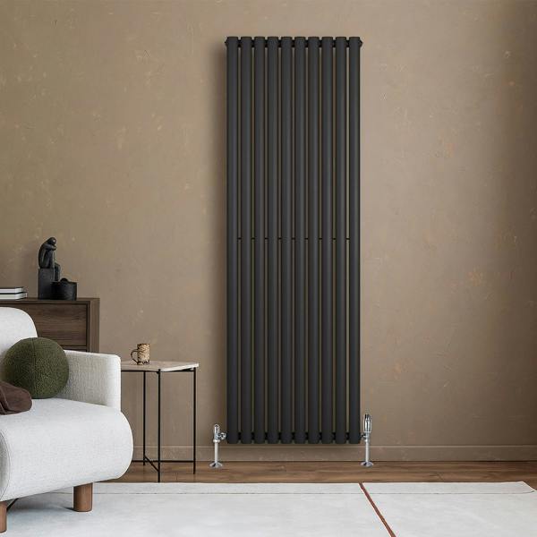 Sleek black oval single column radiator mounted on a textured beige wall, complemented by modern valves and minimalistic decor