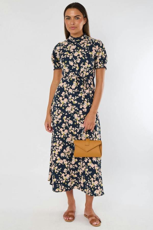 Woman wearing a floral dress holding a brown clutch against a white background