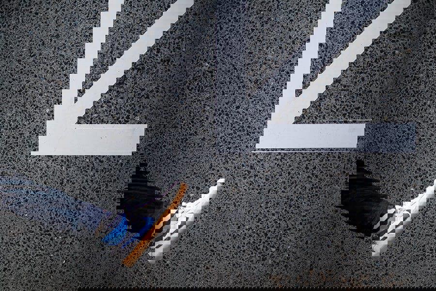 Person wearing white sneakers and bold stripey socks with a blue swoosh logo stepping onto a white arrow on a black asphalt surface.