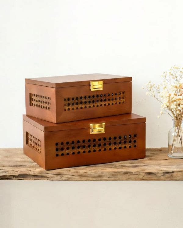 Two wooden storage boxes with lattice designs on a surface with a plant in the background.