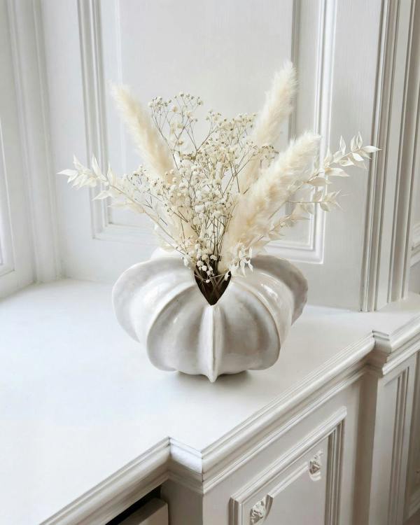 White ceramic vase with dried flowers on a white surface