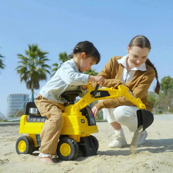 Yellow ride-on digger toy with black wheels and shovel attachment, child playing in sand