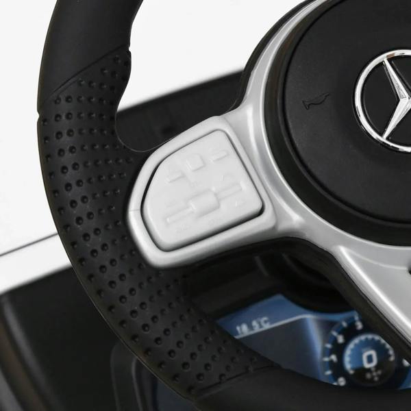 Black textured steering wheel with control buttons and pedals on white kids ride-on car