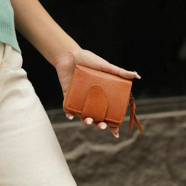 Person holding a cognac leather wallet against a blurred background