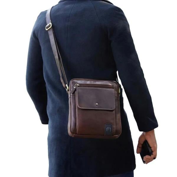 Person wearing a dark coat with a brown leather crossbody bag on a white background