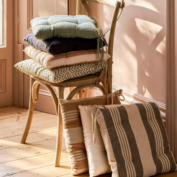 A stack of various linen seat pads on a wooden chair.