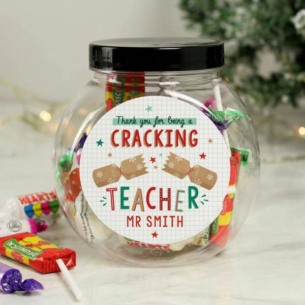 A clear plastic sweet jar filled with Swizzels sweets reading Thank you for being a cracking teacher Mr Smith, with loose sweets on a marble surface.