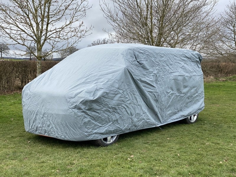 The VW T25/T3/T4/T5/T6 Campervan Cover Grey by OLPRO on a VW T5 Campervan with bushes and trees in the background.