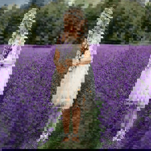 Young girl in a floral dress holding lavender in a field of purple flowers.