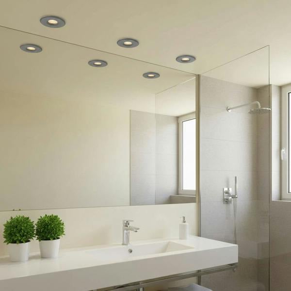 Mini ceiling spotlight above a bathroom sink with plants and a shower to the right of the sink