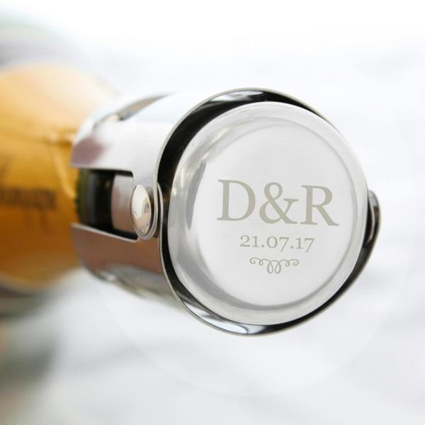 A polished silver stainless steel bottle stopper engraved with 'D&R' and '21.07.17' clamping the top of a champagne bottle.