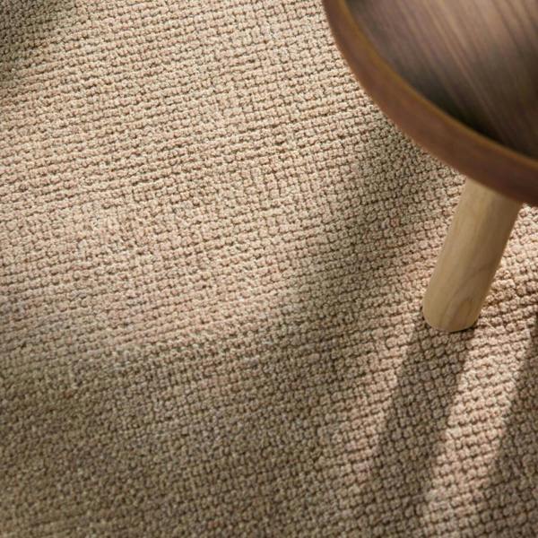 Close-up of a textured beige carpet with a wooden leg partially visible