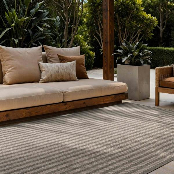 Outdoor seating area with a striped rug, cushions, and plants.