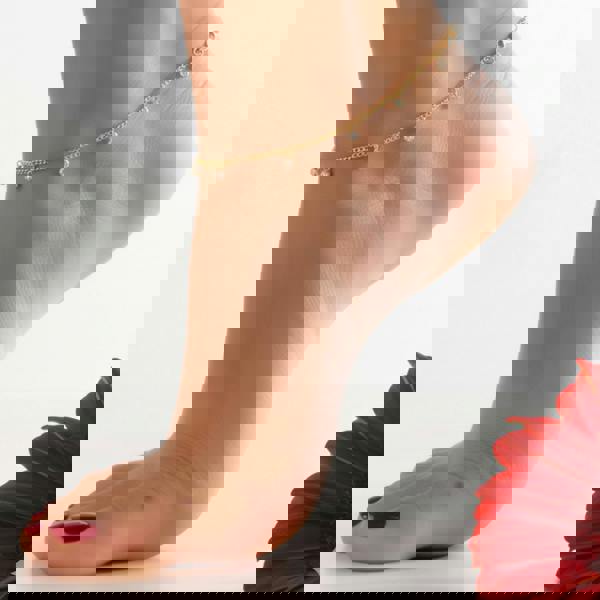 close-up shot of the Illuminess™ Apah Water Goddess Anklet in premium gold vermeil, modeled on an olive-toned ankle. The dainty silver chain features shimmering lab-diamond droplets that catch the light, creating a liquid-sparkle effect