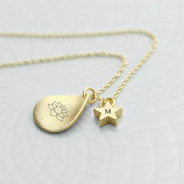 A gold-plated personalised lotus pendant necklace with an engraved initial star charm resting on a textured surface.