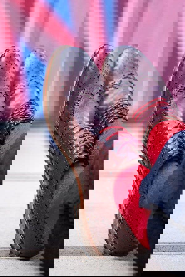 Brown leather shoes with red laces and red socks against a blurred background