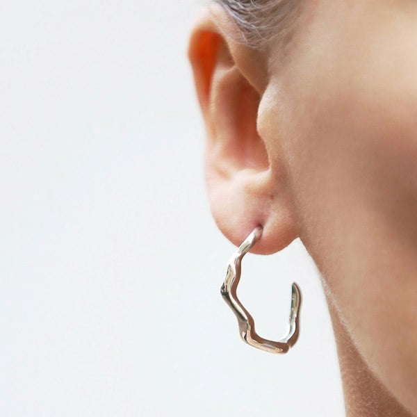 A close up of silver wavy hoop earring in an ear.