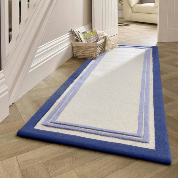 White rug with blue border on a wooden floor next to a staircase