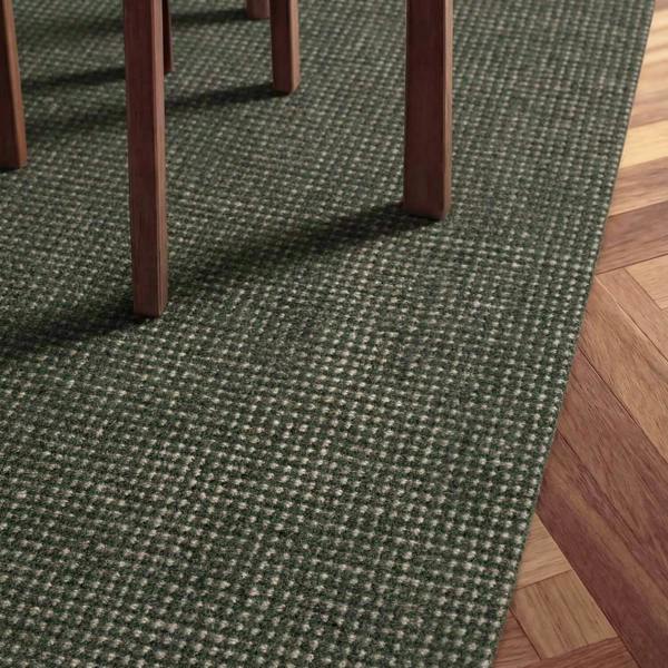 Green textured carpet with wooden floor and chair legs