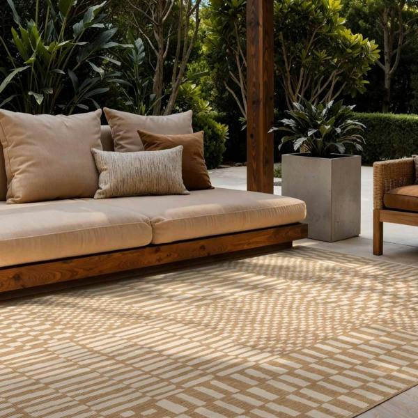 Beige outdoor sofa with cushions on a patterned rug in a garden setting