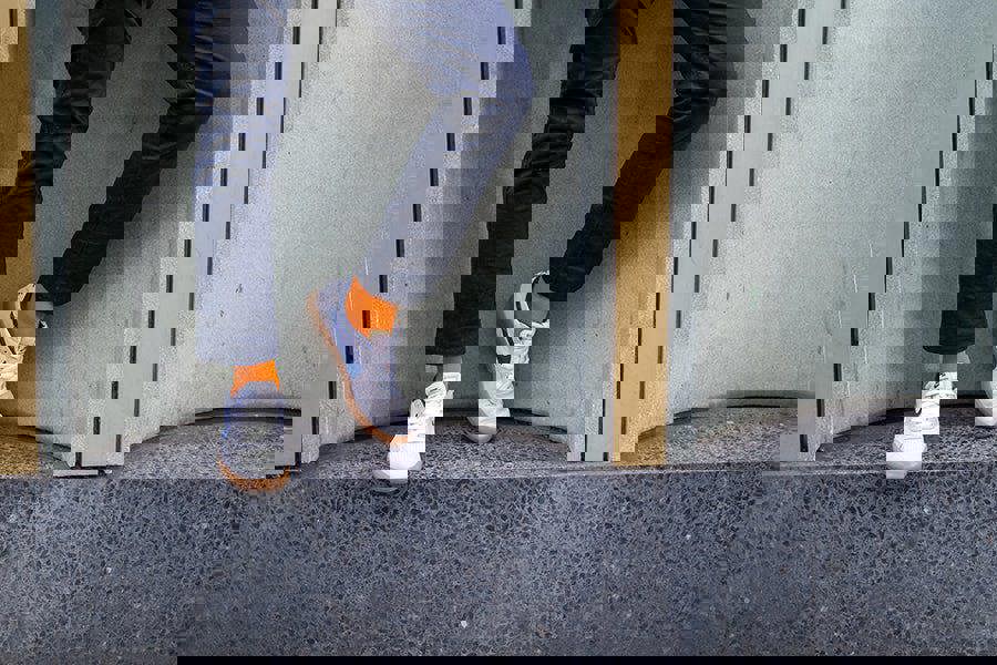 Person wearing navy pants, white sneakers with orange socks, standing on a ledge.