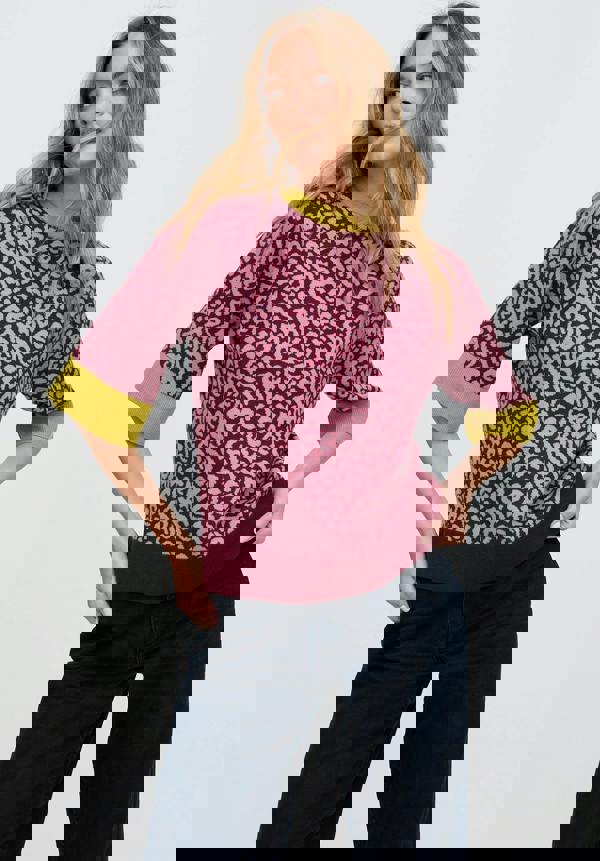 Woman wearing a pink leopard print sweater with green cuffs and hem on a white background