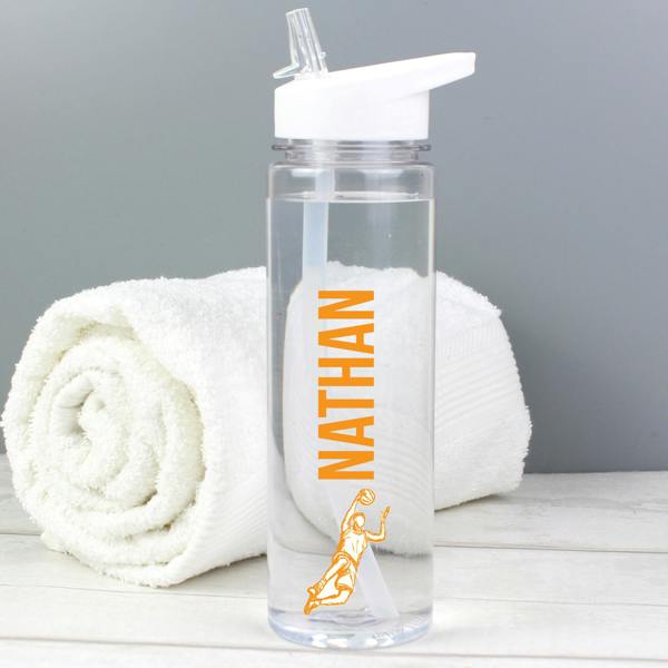 A transparent 750ml sports water bottle custom-printed with the name 'Nathan' in vibrant orange vertical font above a male basketball player graphic, positioned in front of a rolled white towel.