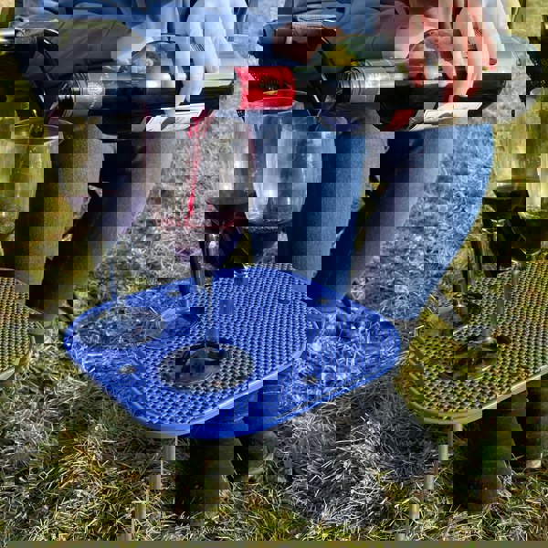 Close-up image of OLPRO Camping Spike Stick Table outside a tent with a glass of wine on top, showing the non-slip matting.