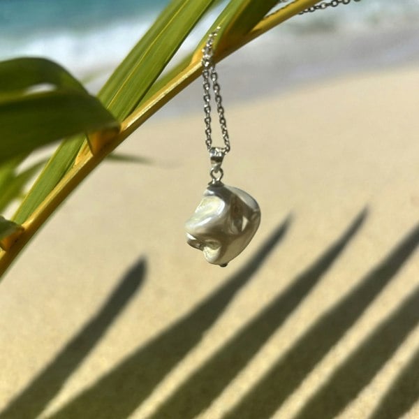 Natural shell pendant charm displayed on an exotic Cayman Islands beach.