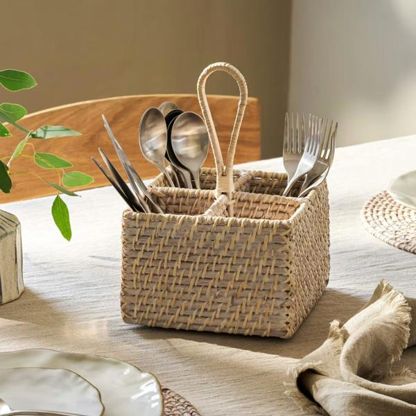 Whitewash rattan cutlery caddy with four sections and a loop handle styled on a dining table.