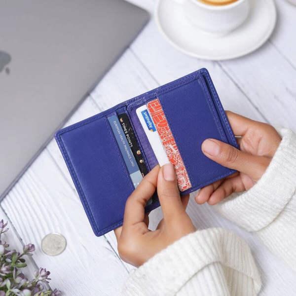 Person holding a purple wallet with cards on a desk with a cup of coffee.
