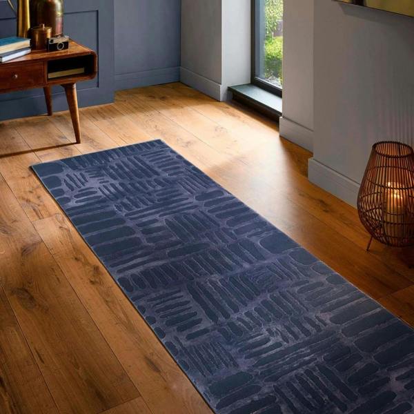 Blue patterned rug on a wooden floor in a room with a window and lamp.